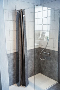 Moderne Eckdusche mit Glasabtrennung, grauem Duschvorhang und grauen Wandpaneelen.