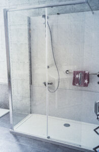 Moderne, barrierearme Dusche mit Glas-Schiebetüren, Handbrause und Haltegriff mit Handtuchhalter.