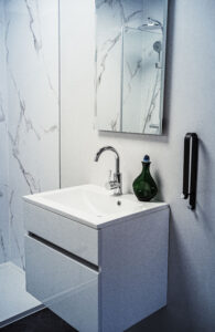 Modernes weißes Waschbecken mit Chromarmatur, Spiegel, grüner Vase und Handtuchhalter an der Wand.