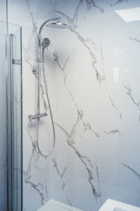 Moderne Dusche mit großem Regenduschkopf, Handbrause und Wandverkleidung in weißer Marmoroptik mit grauen Adern.
