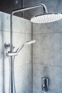 Nahaufnahme einer modernen Dusche mit großem runden Regenduschkopf und Handbrause vor grauen Wandfliesen.