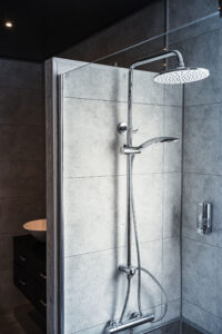 Moderne Dusche mit großen grauen Fliesen, verchromtem Regenduschkopf und Handbrause.