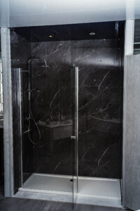 Moderne Dusche mit schwarzen Marmorwänden, Glasdrehtür und Regendusche.