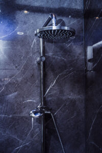 Nahaufnahme einer modernen Regendusche mit zusätzlicher Handbrause vor einer dunklen Marmorwand mit weißen Adern.