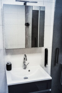 Waschbecken mit verchromter Armatur, schwarzem Seifenspender und großem Spiegelschrank in einem modernen Badezimmer.