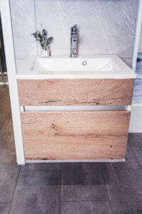 Modernes Waschbecken mit Unterschrank in Holzoptik vor grauer Marmorwand.