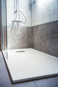 Ebenerdige Dusche mit grauer Steinoptik-Wandverkleidung, Glasabtrennung und moderner Handbrause.