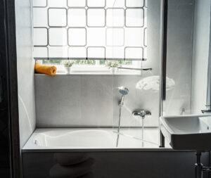 Moderne Badewanne mit seitlicher Duschabtrennung, Handbrause und Fensterbank mit Pflanzen und Handtuch.