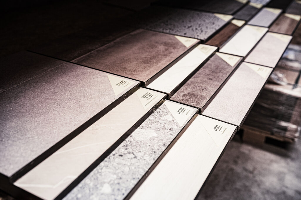 Verschiedene Fliesenmuster in unterschiedlichen Farben, Texturen und Oberflächenstrukturen, geordnet auf einer Ausstellungsfläche.