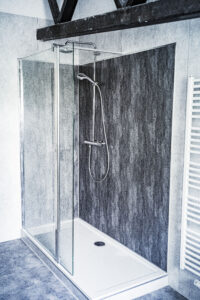 Moderne Eckdusche mit Glasabtrennung, grauer Steinoptik-Wandverkleidung, Regendusche und Handbrause, eingebaut unter einer offenen Dachbalkenkonstruktion.