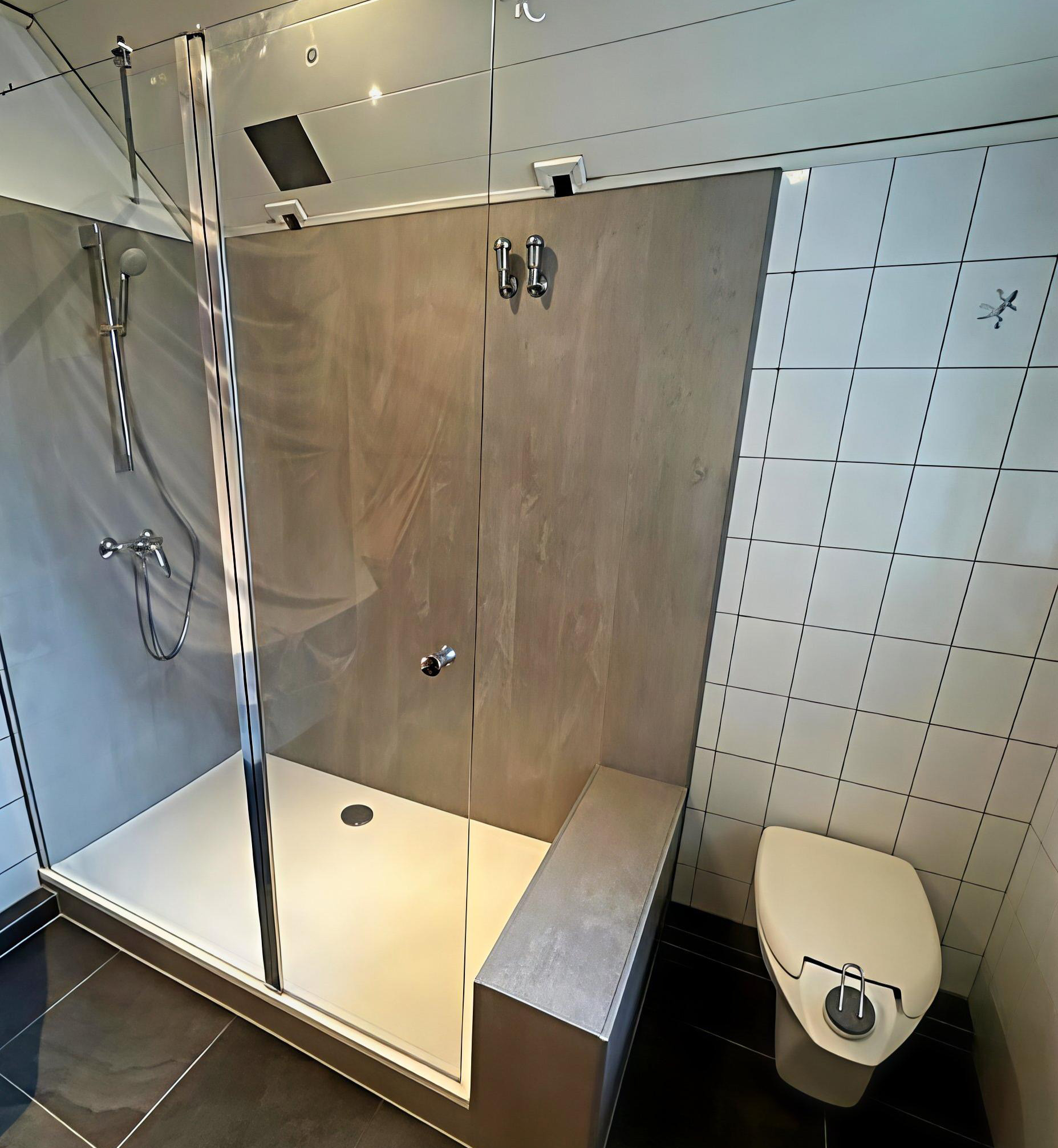 Moderne, barrierearme Dusche mit großer Glasabtrennung, integrierter Sitzfläche, Handbrause und hellen Wandverkleidungen in Holzoptik, neben einem wandhängenden WC.