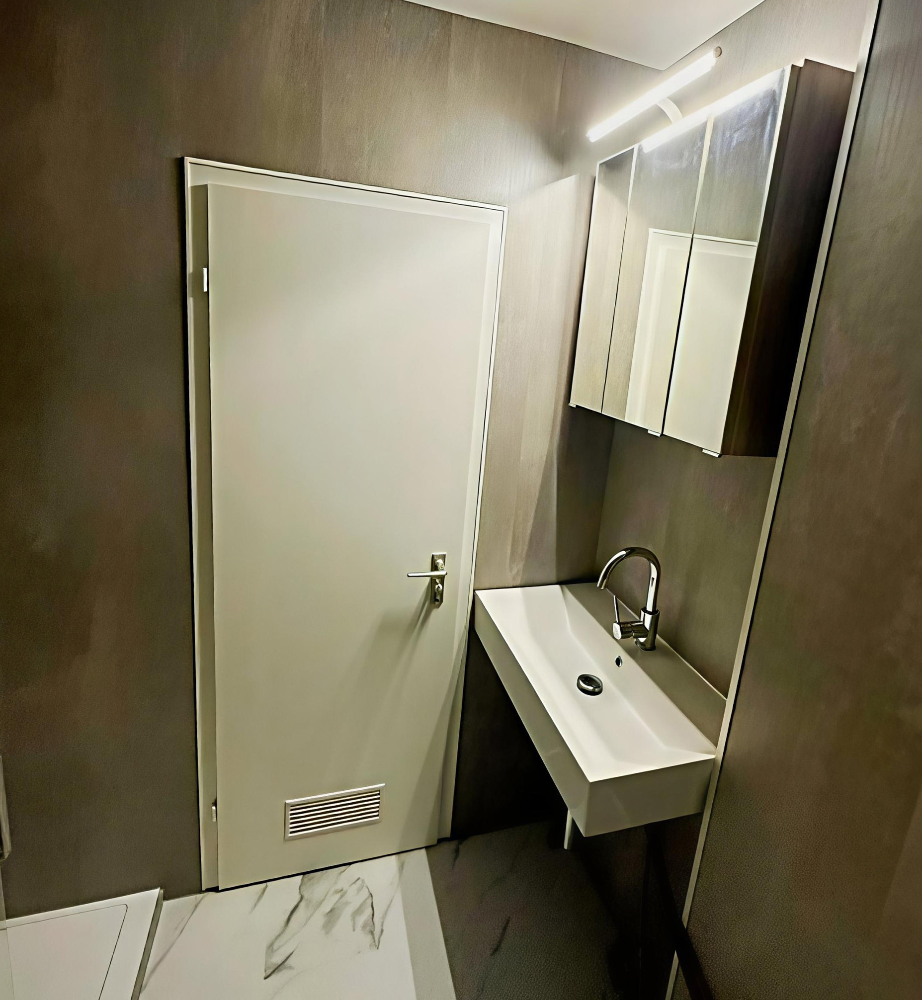 Modernes, barrierearmes Bad mit unterfahrbarem Waschbecken ohne Unterschrank, Einhebelmischer für einfache Bedienung, Spiegelschrank mit LED-Beleuchtung und grauer Wandverkleidung.