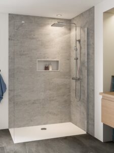 Barrierearme Walk-In Dusche mit grauer Wandverkleidung in Betonoptik, Regenduschkopf, Handbrause und integrierter Nischenablage für Duschutensilien.