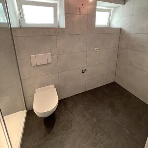 Modernes Bad mit wandhängendem WC, grauer Wandverkleidung und dunklem Boden; Teilsanierung von novaDUSCH.